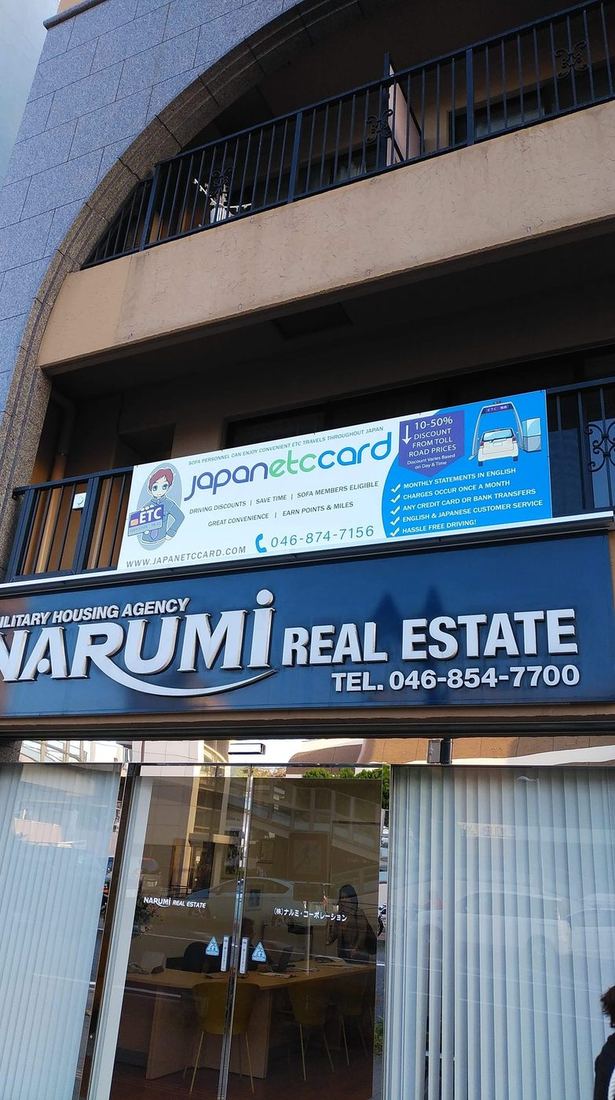2018年新拠点の正面 ─ NARUMI不動産入口の上に大きく掲げられた、英語で利用メリットを案内するJapanETCcardの広告バナー（SOFA会員向け）。